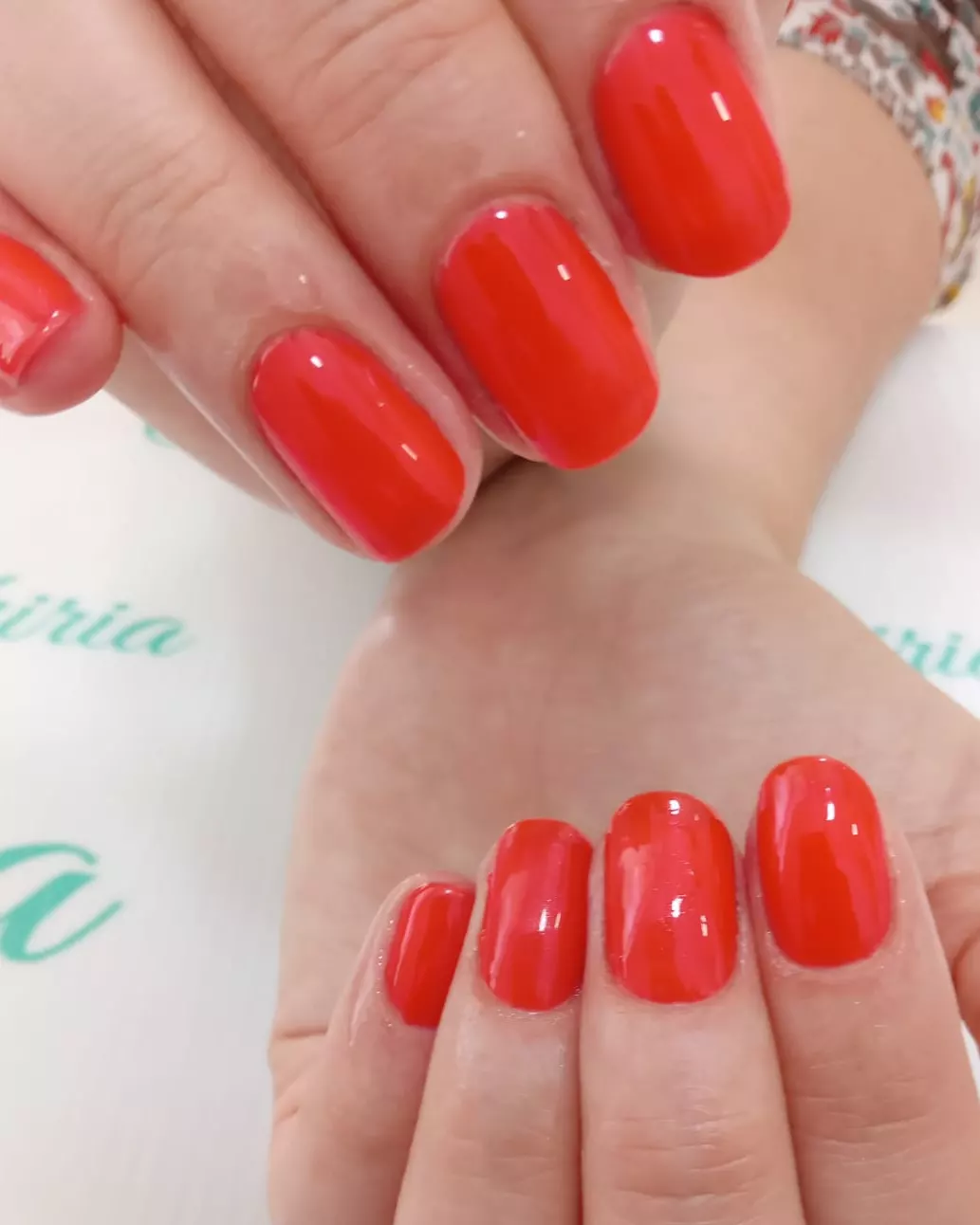 Manos con esmaltado rojo brillante sobre el mantel blanco con el logo turquesa de Valkiria