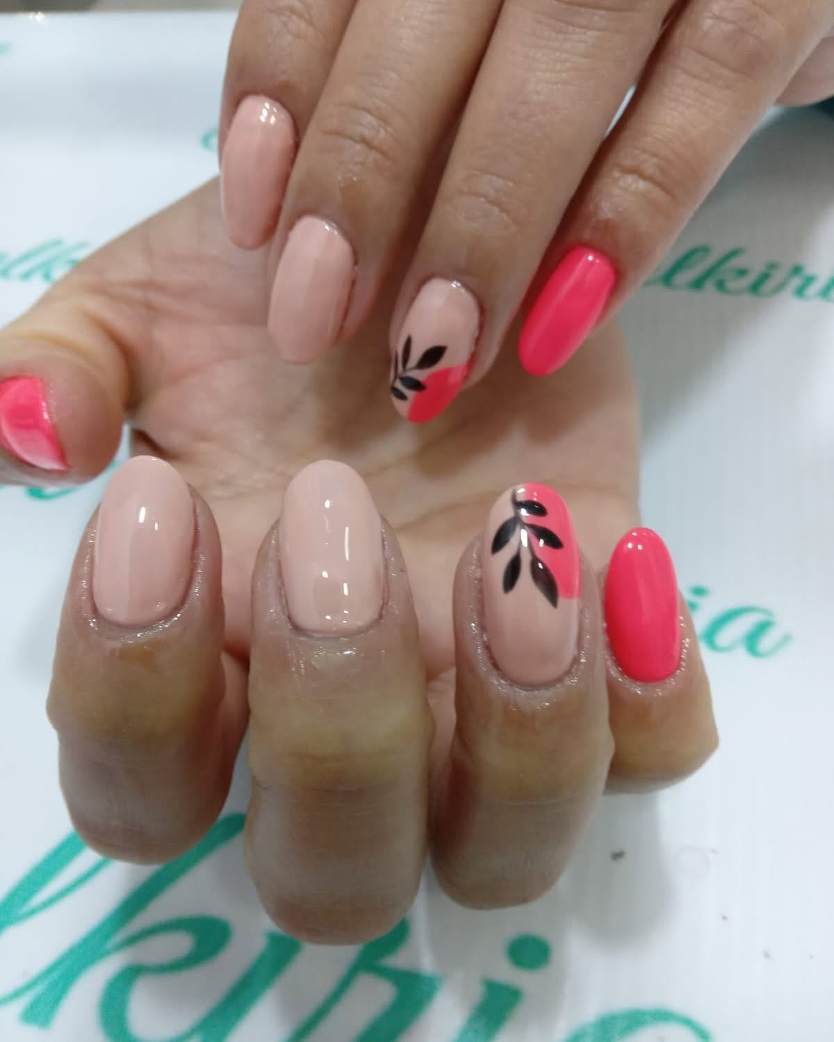 Uñas almendradas en nude y coral, con ramitas negras pintadas a mano en dos uñas, sobre el mantel de Valkiria